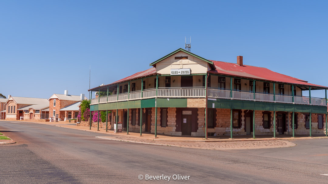 A historic building with a green and red exterior, situated on a corner street, surrounded by other buildings in a town setting. The sky is clear and blue.