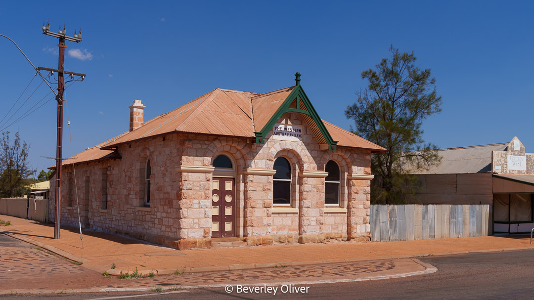 Historic stone building with a red and green roof, labeled as 'The Western Australian Bank', set against a blue sky.
