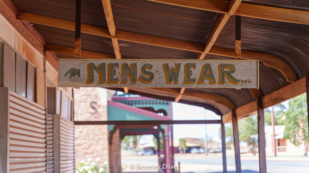 Signage for 'Men's Wear' hanging under a covered walkway.