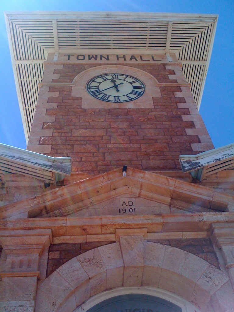 Looking up at the historic Town Hall clock tower with a blue sky in the background, featuring a clock displaying the time and the year marked 'AD 1901' on the facade.