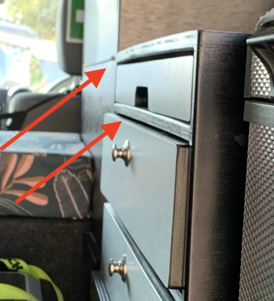 A close-up view of a chest of drawers with arrows pointing at the top drawer and the edge of the unit, set in a vehicle interior.
