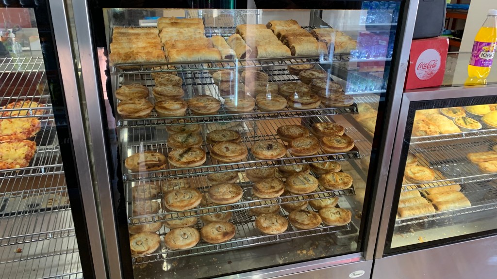 A display case filled with various baked goods, including pastries and meat pies, showcasing different textures and colors.