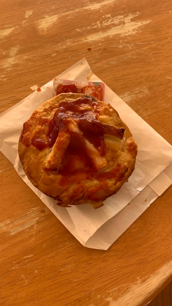 A savory pastry topped with tomato ketchup, resting on a piece of white paper on a wooden table.