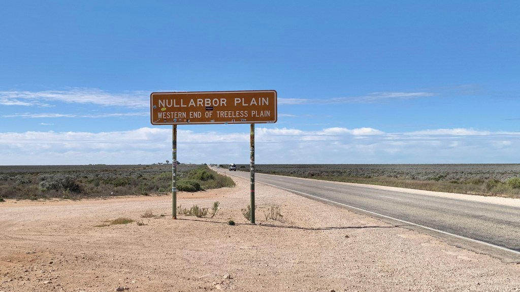 Sign for Nullarbor Plain indicating the western end of the treeless plain, with a wide open landscape and blue sky in the background.