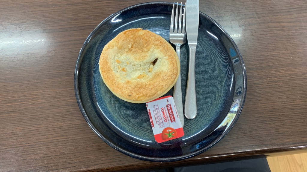 A flaky pastry on a dark blue plate with a small container of tomato sauce, alongside a fork and knife.